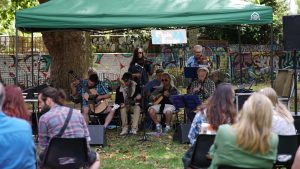 Group of people playing music under a green awning in the park